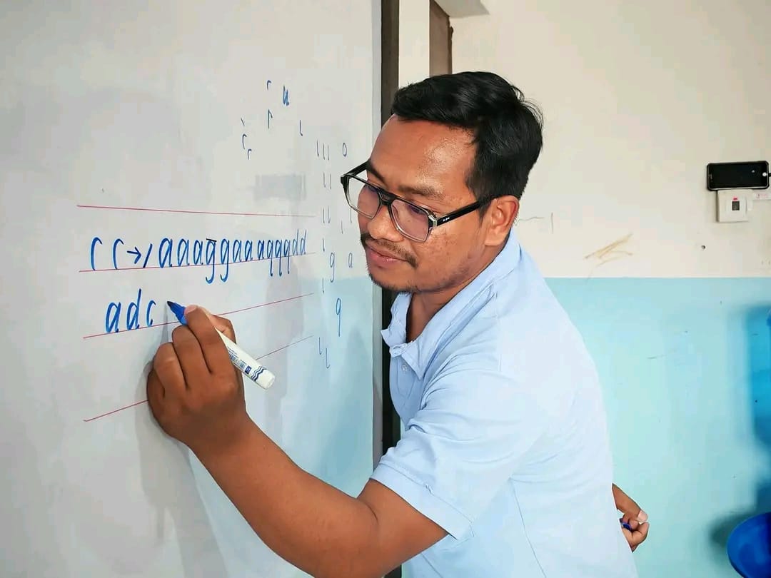 Teacher demonstrating cursive letters on a lined whiteboard during a handwriting class